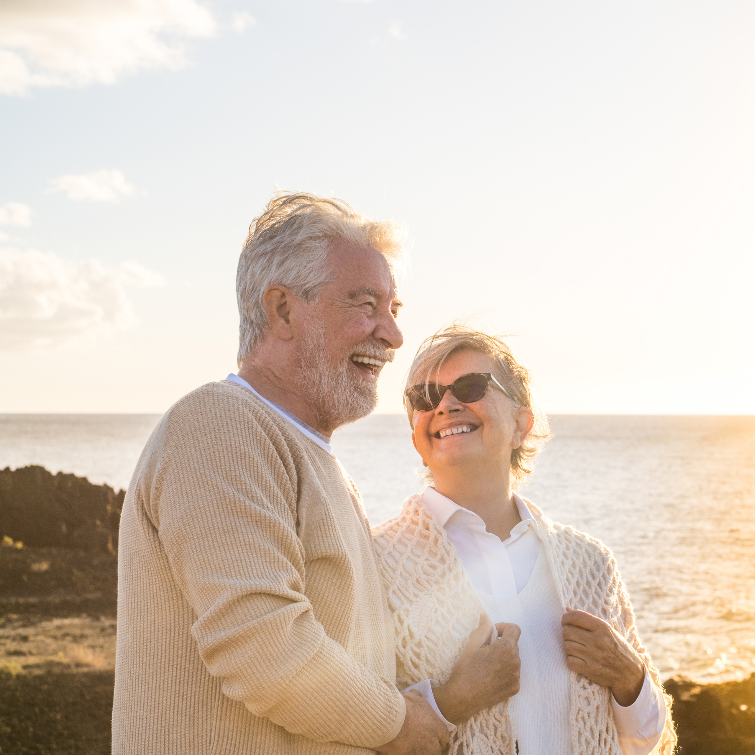 a couple walking near the shoreline and holding each other while smiling, with sunbeams streaming in from the sky over the ocean