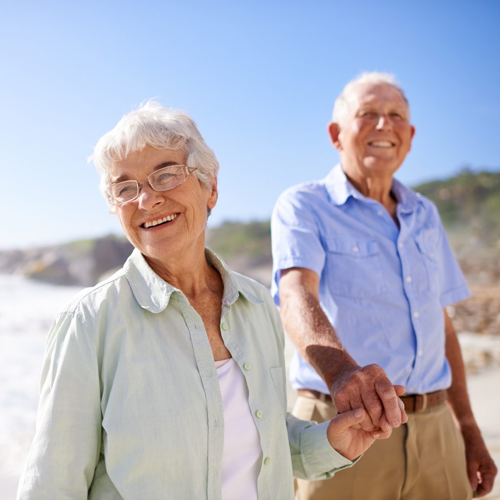 a resident couple gaze out towards the water from a sandy beach, with satisfied smiles on their faces, and hands held between them
