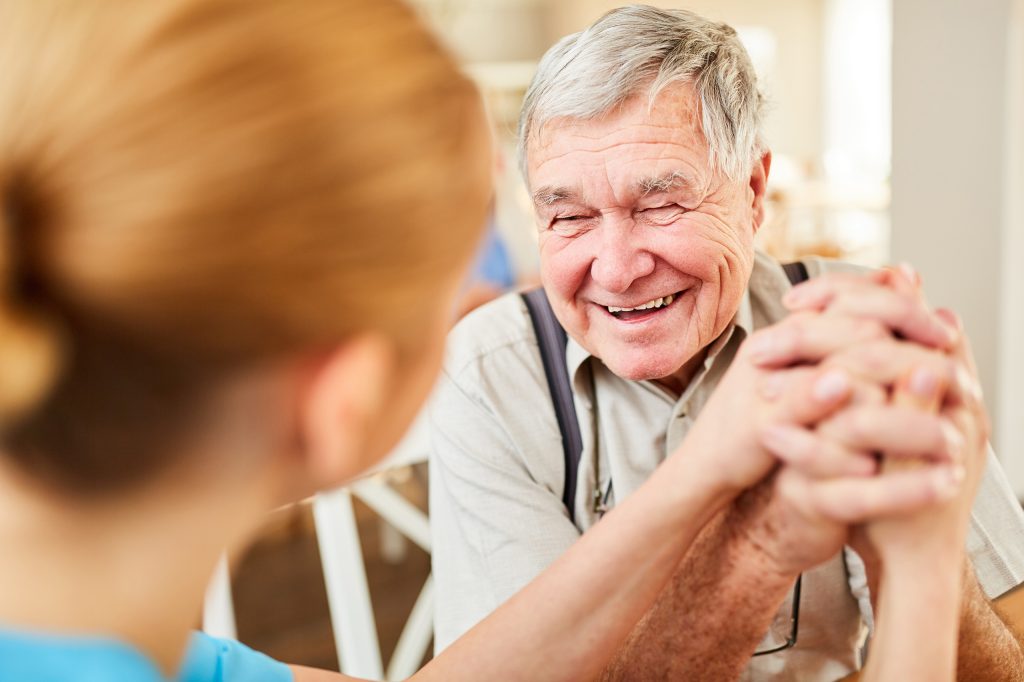 a resident smiles and holds hands with a younger person who is facing away from view