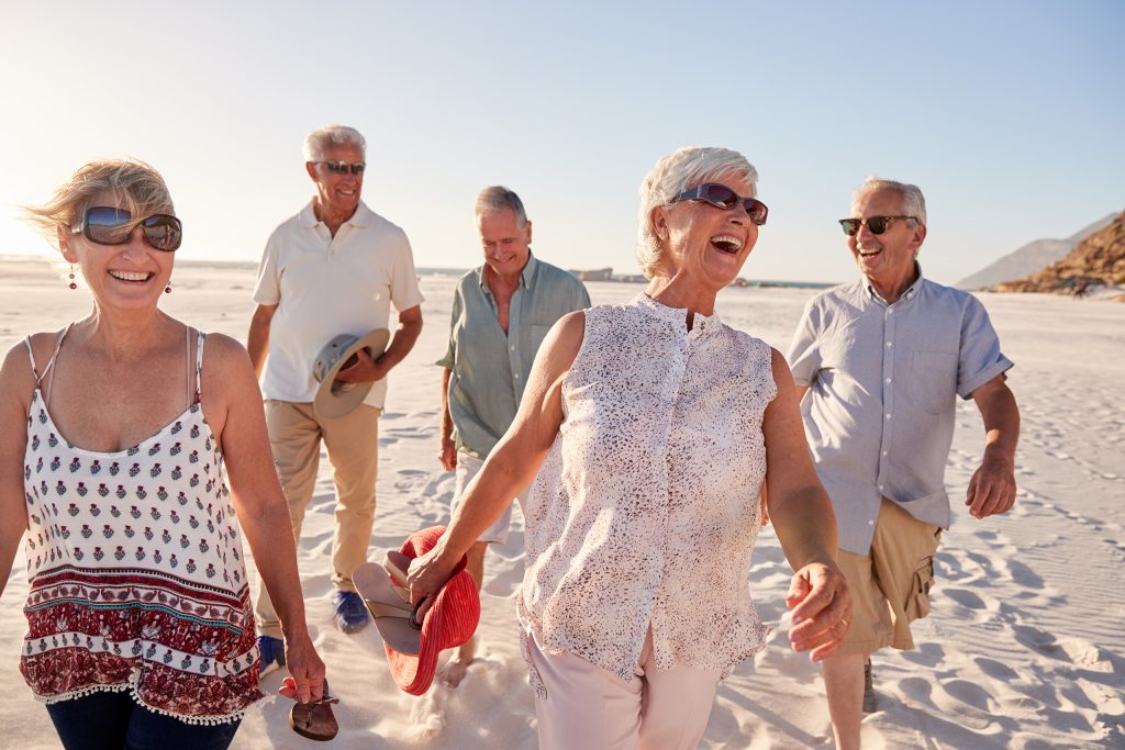 five people are walking on a sandy beach, laughing and holding their sandals in their hands