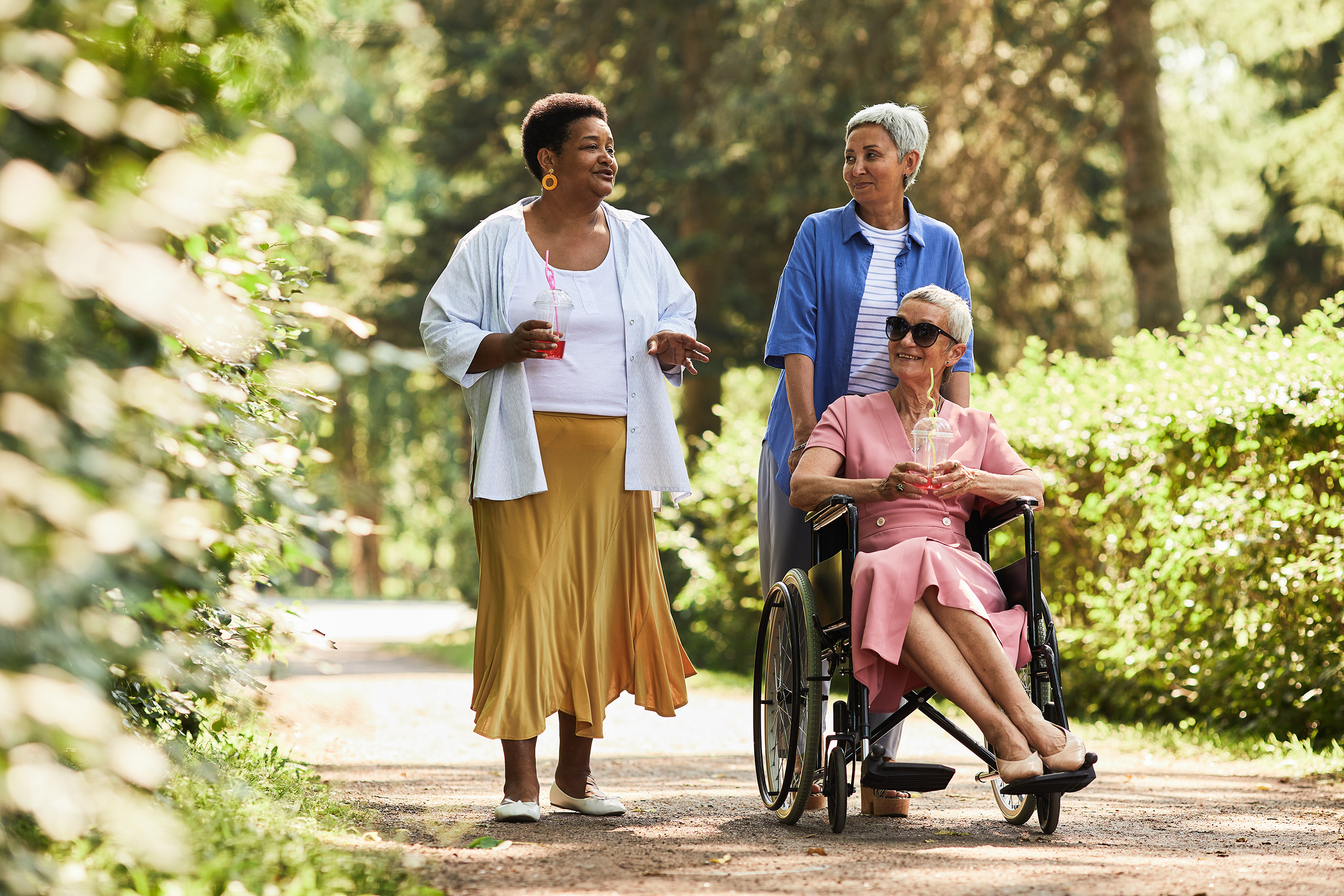 three residents, one in a wheelchair, share a conversation and a stroll on a path through greenery