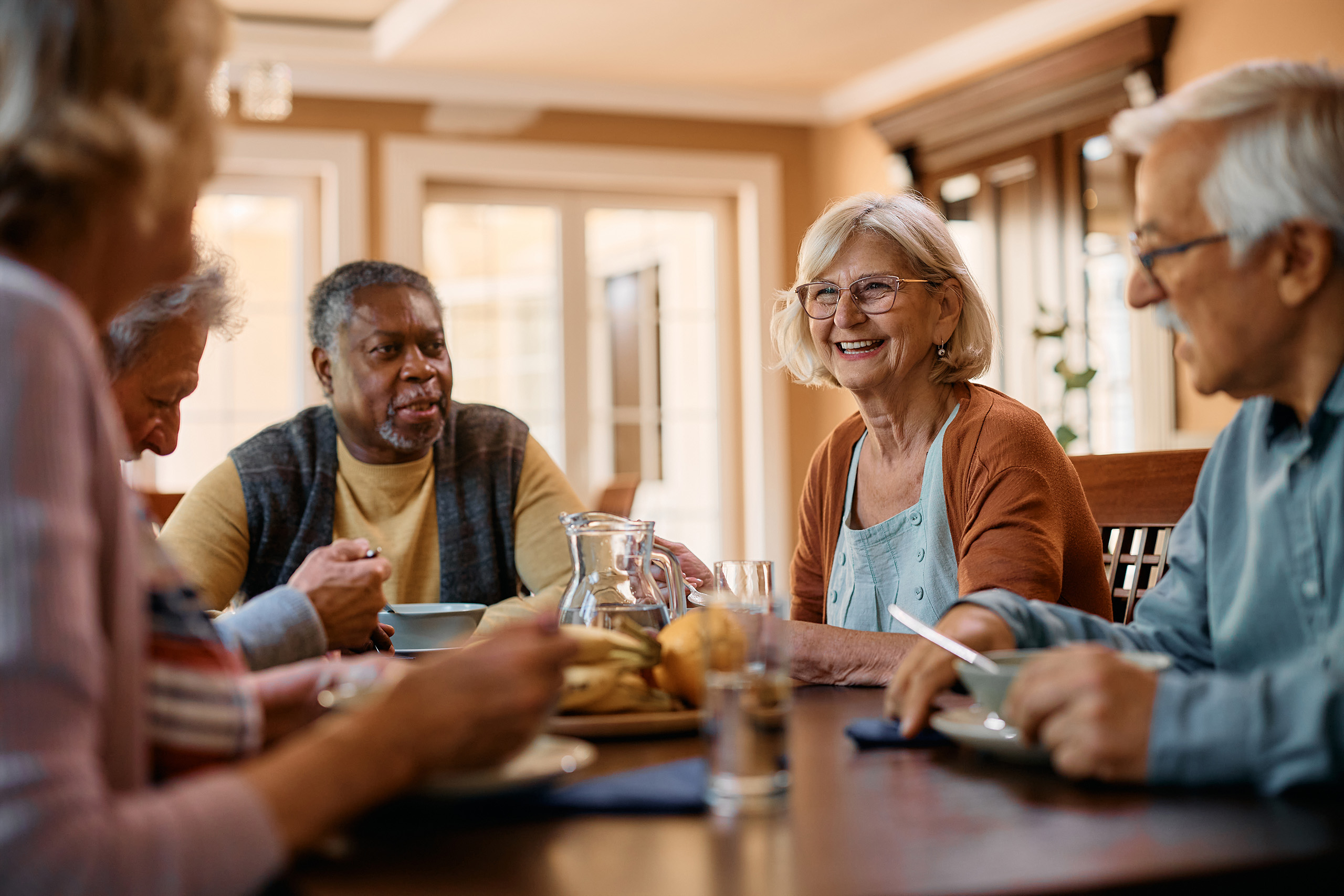 five residents sit around a table indoors, sharing a conversation over a meal