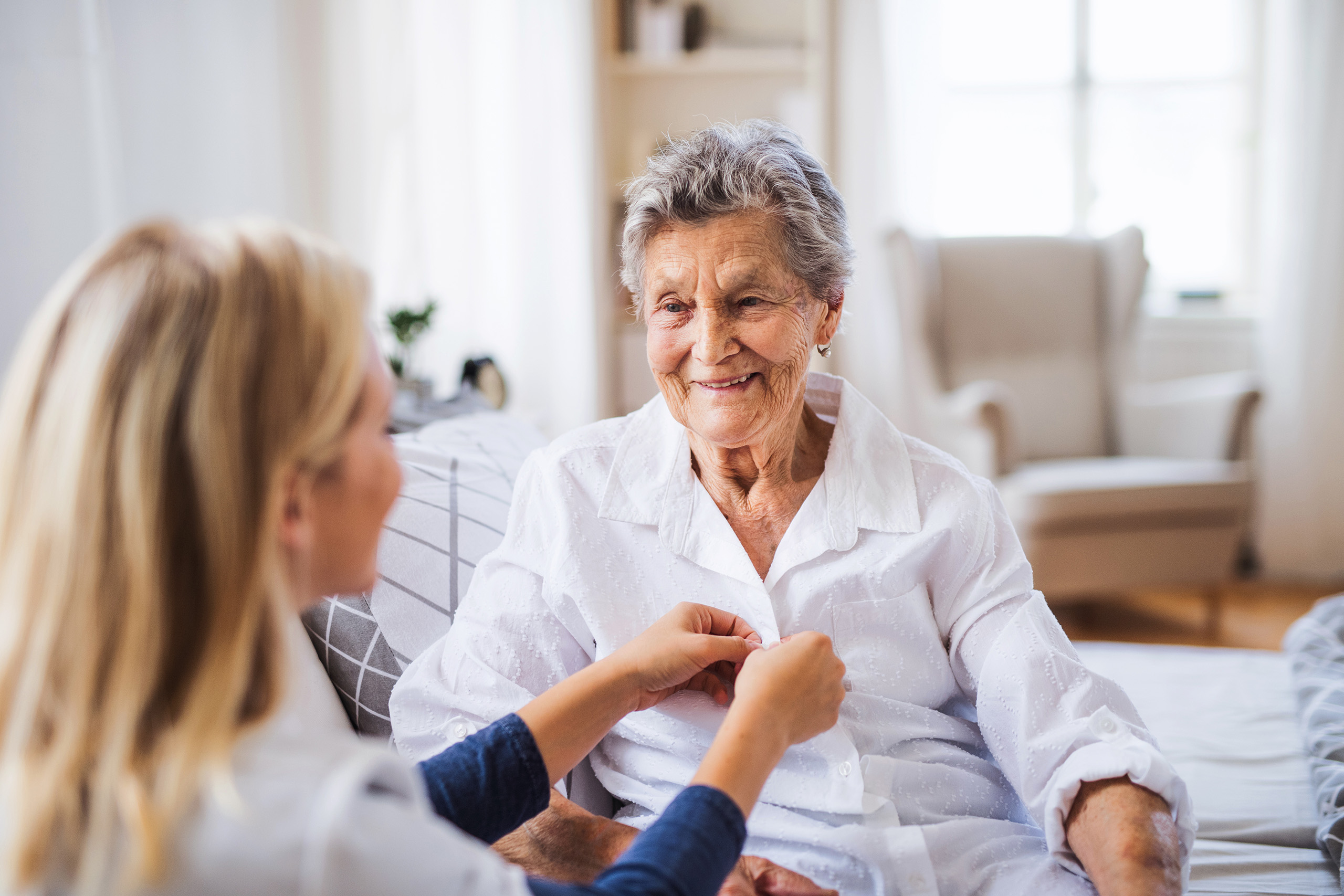 a care employee helps an elderly resident with their shirt; the setting is the resident's home